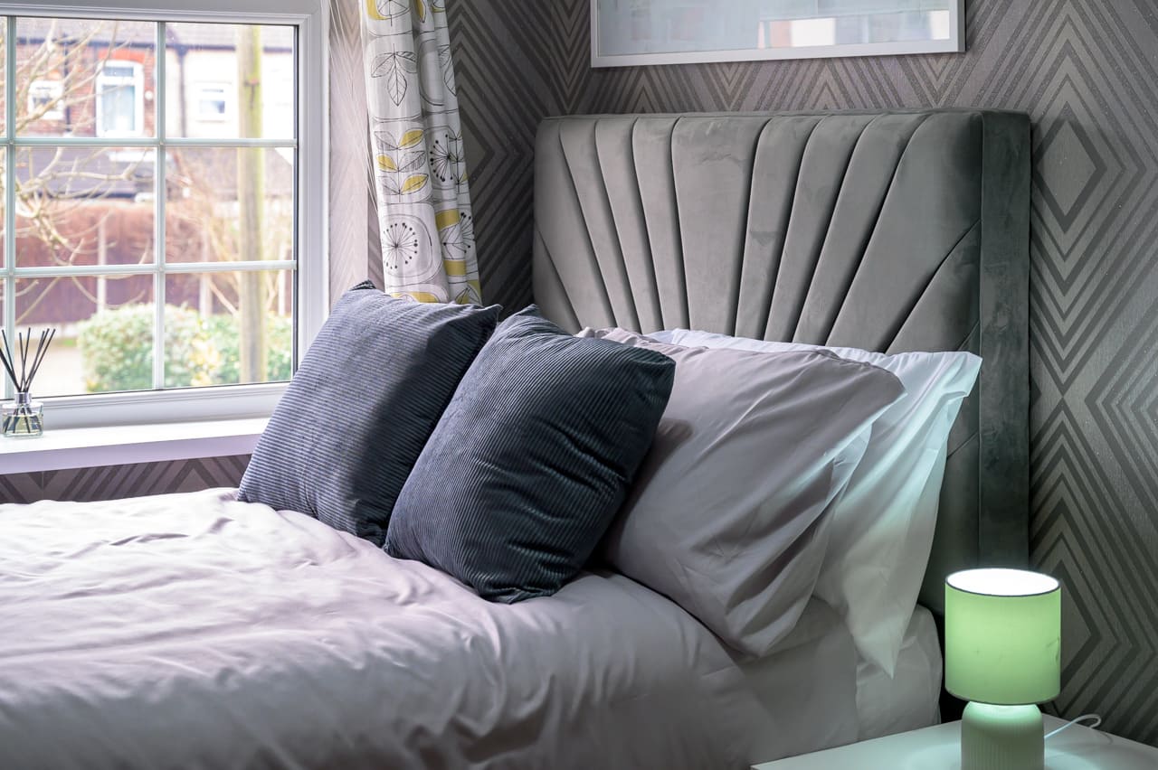 Grey velvet fan-shaped headboard on a bed with pillows and patterned wallpaper