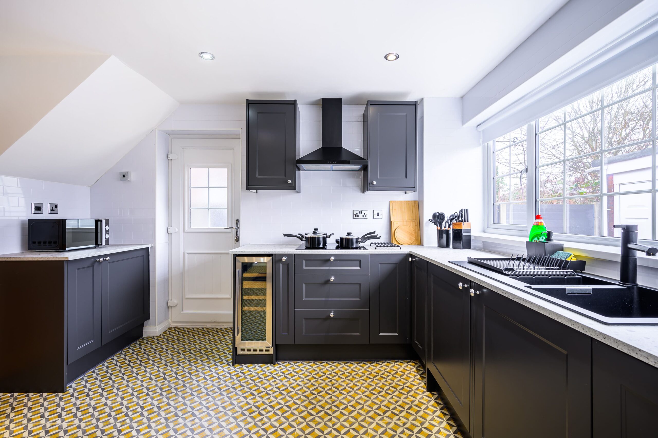 Modern kitchen with dark grey cabinets, white tiled walls, and a yellow and grey patterned floor
