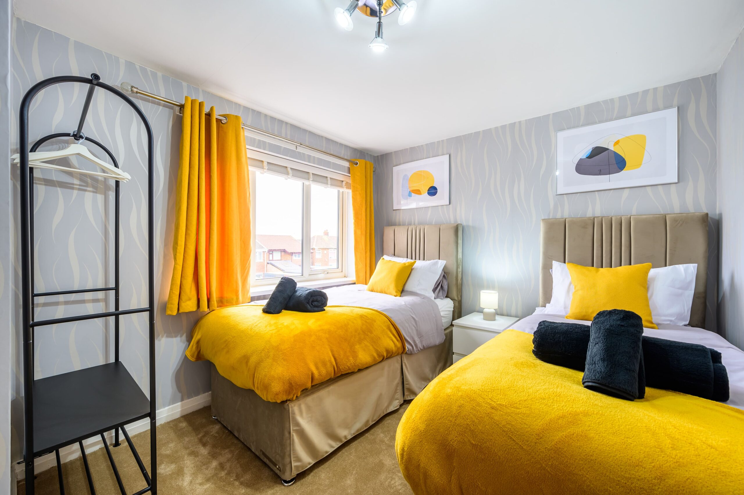 Twin bedroom with yellow throws, black towels, and grey patterned wallpaper