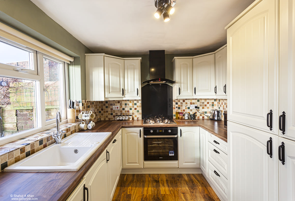 Modern kitchen with cream cabinets, dark wood worktops, mosaic splashback, and integrated black oven and hob