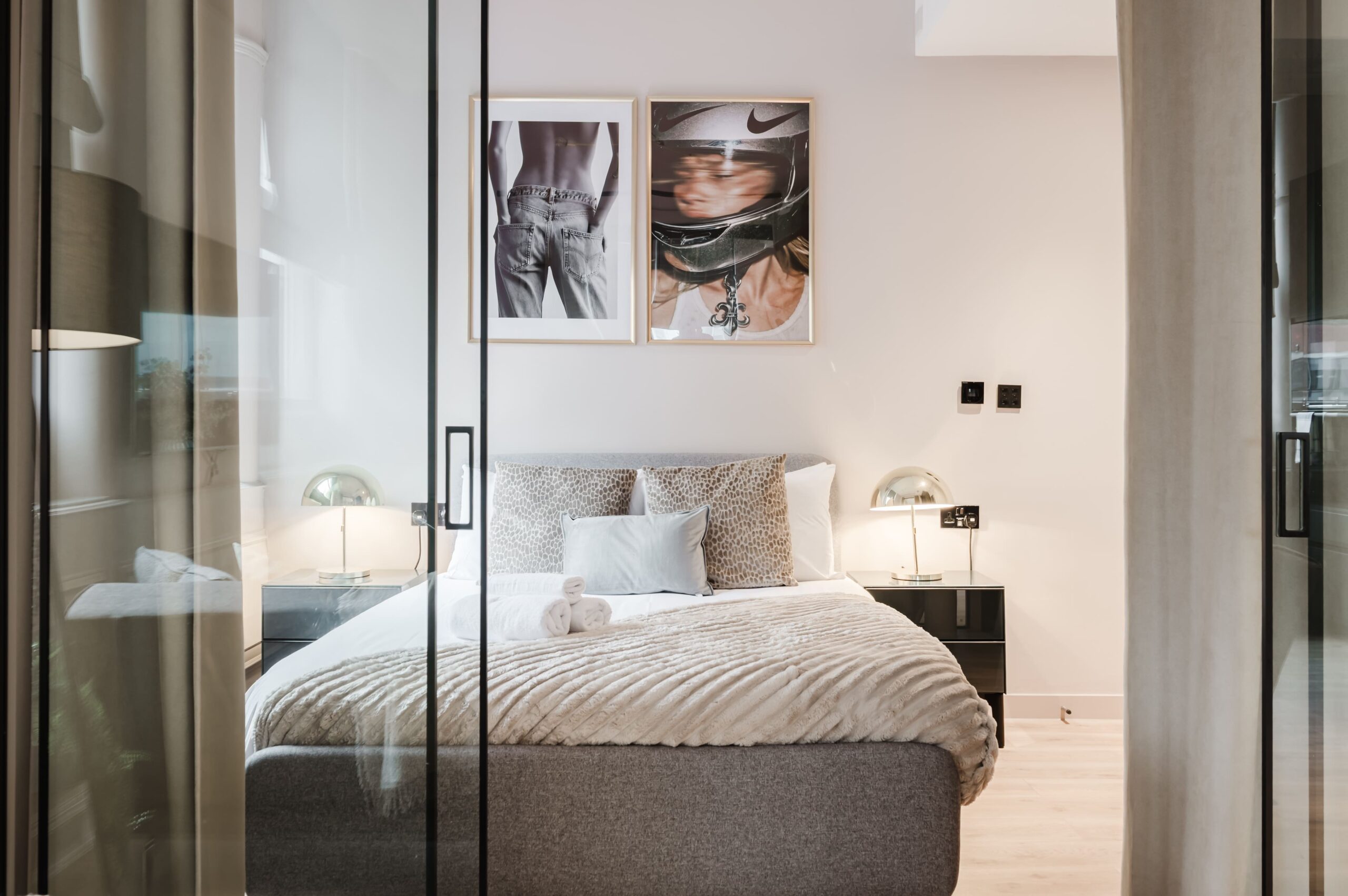 Modern bedroom with a grey fabric bed, patterned cushions, and two framed photos on the wall
