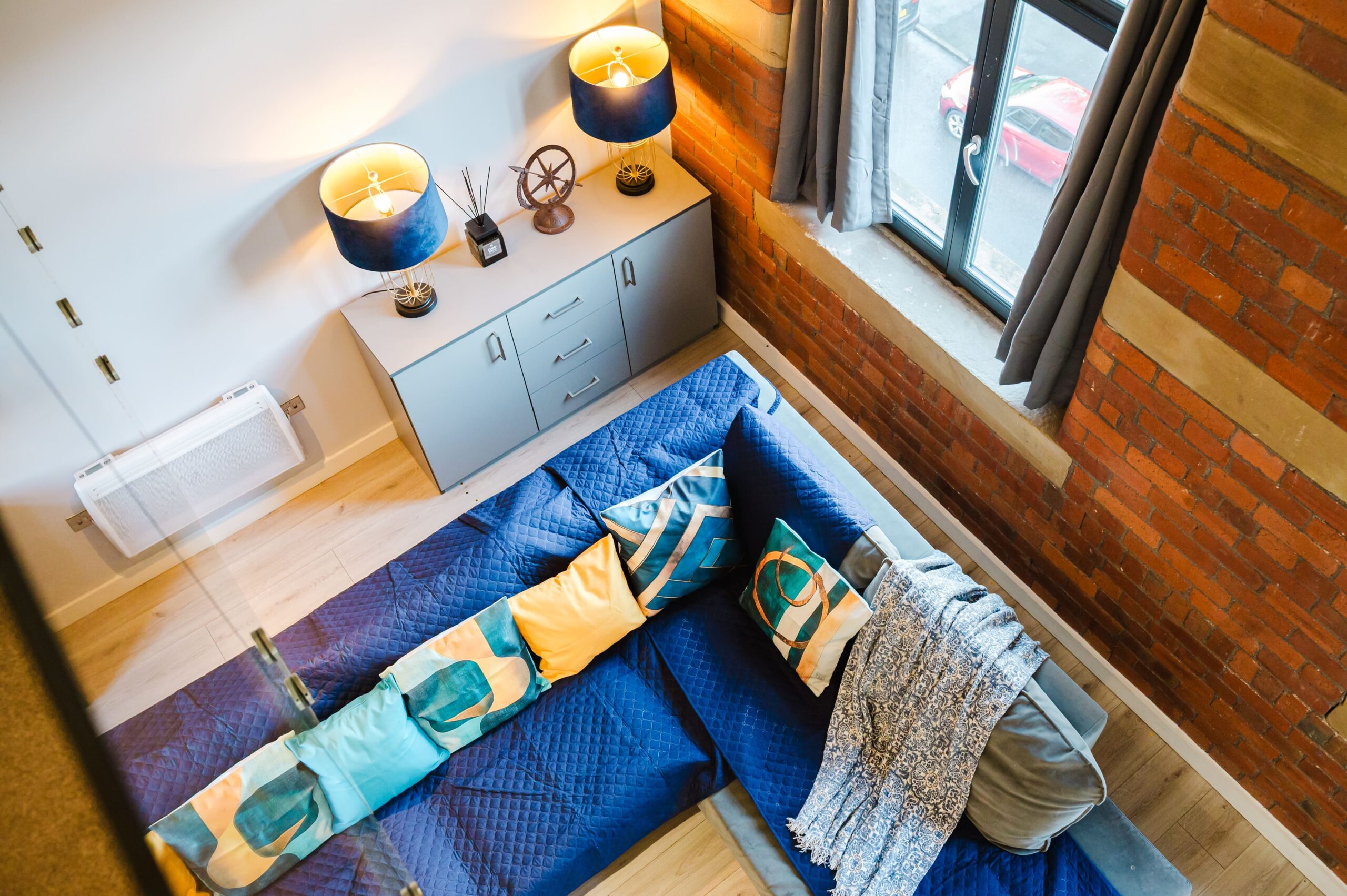 High-angle view of a blue sofa with colourful cushions, a grey sideboard, and an exposed brick wall
