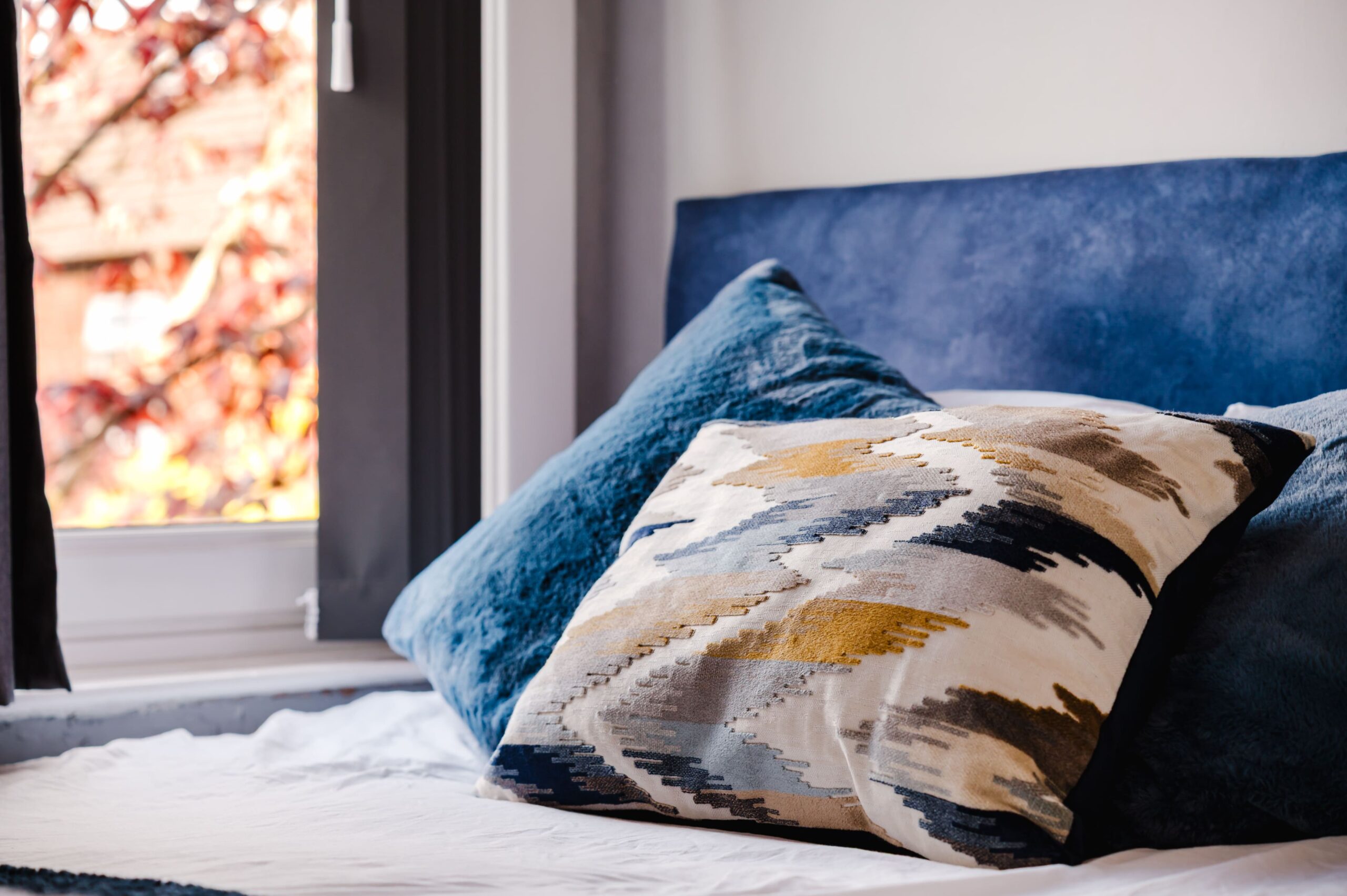 Blue velvet headboard and cushions on a bed, with a patterned cushion in yellow, grey, and blue