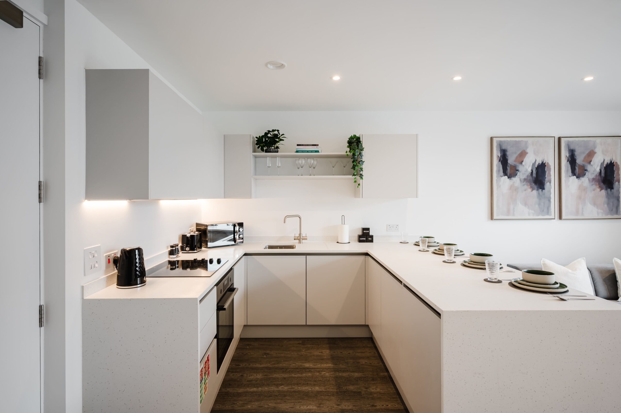 Modern white U-shaped kitchen with dark wood floors and a breakfast bar set for four