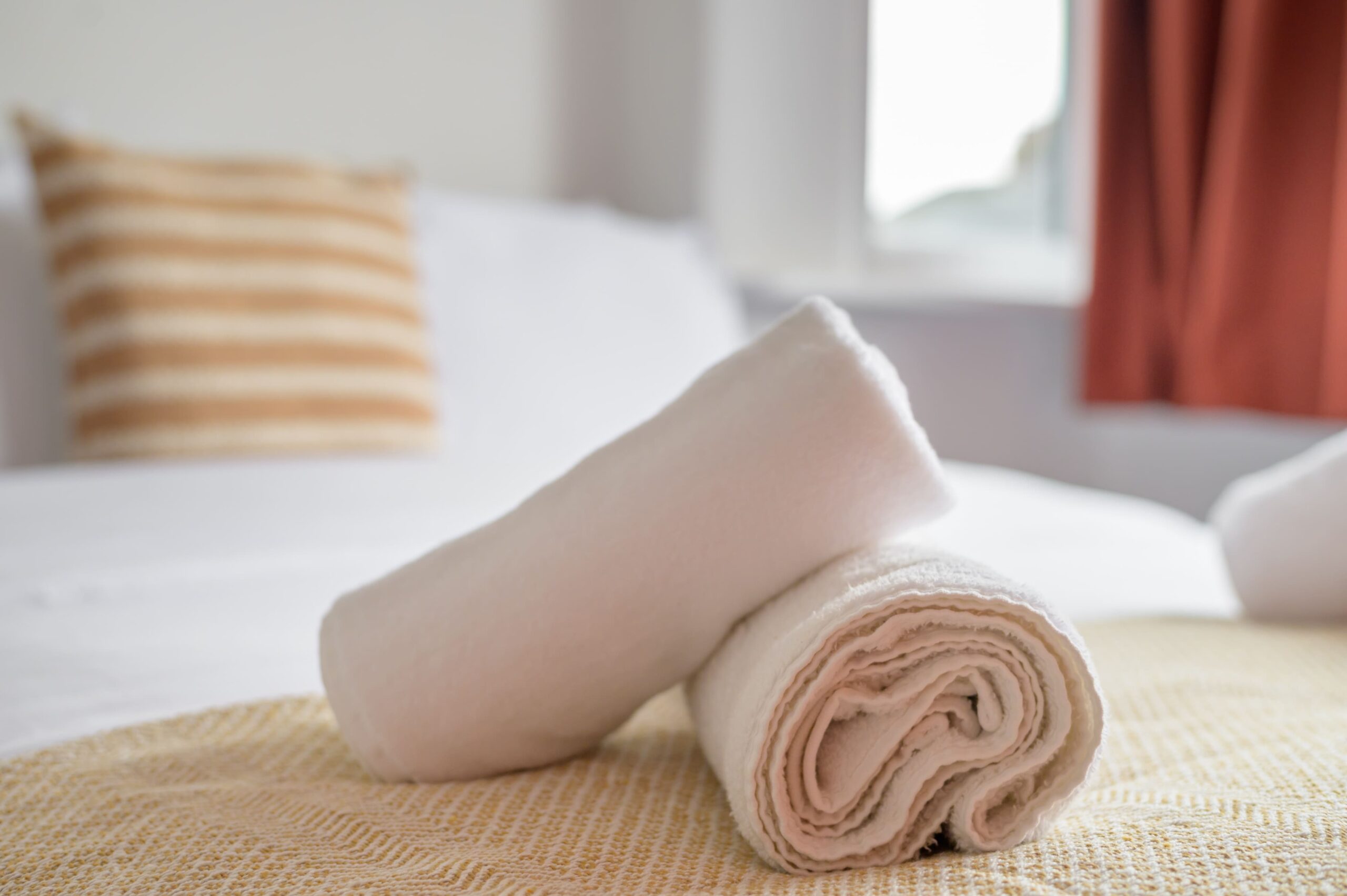 Two rolled white towels on a bed with a yellow patterned throw