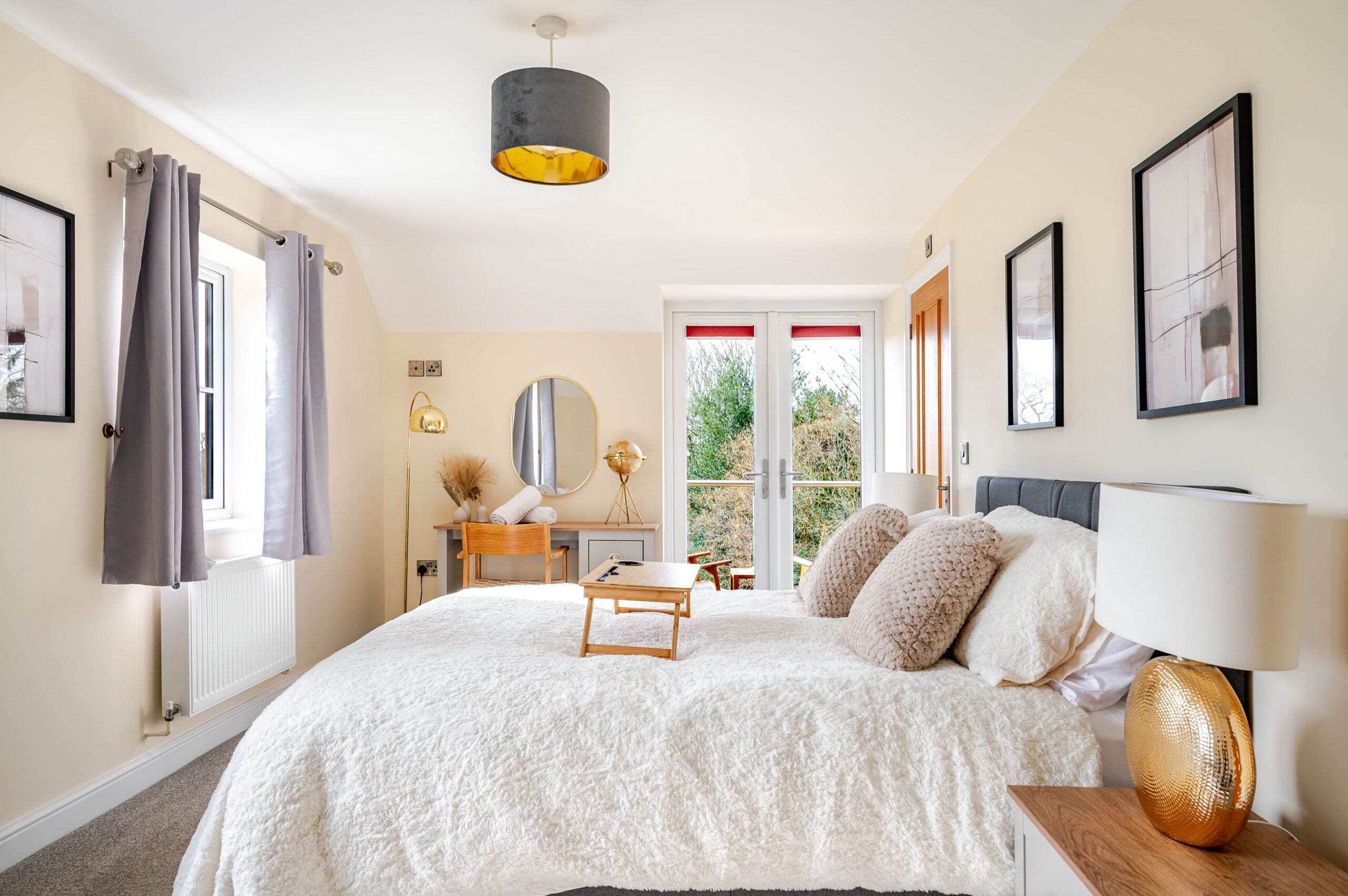 Bright bedroom with white textured bedding, a dressing table, and French doors leading to a balcony