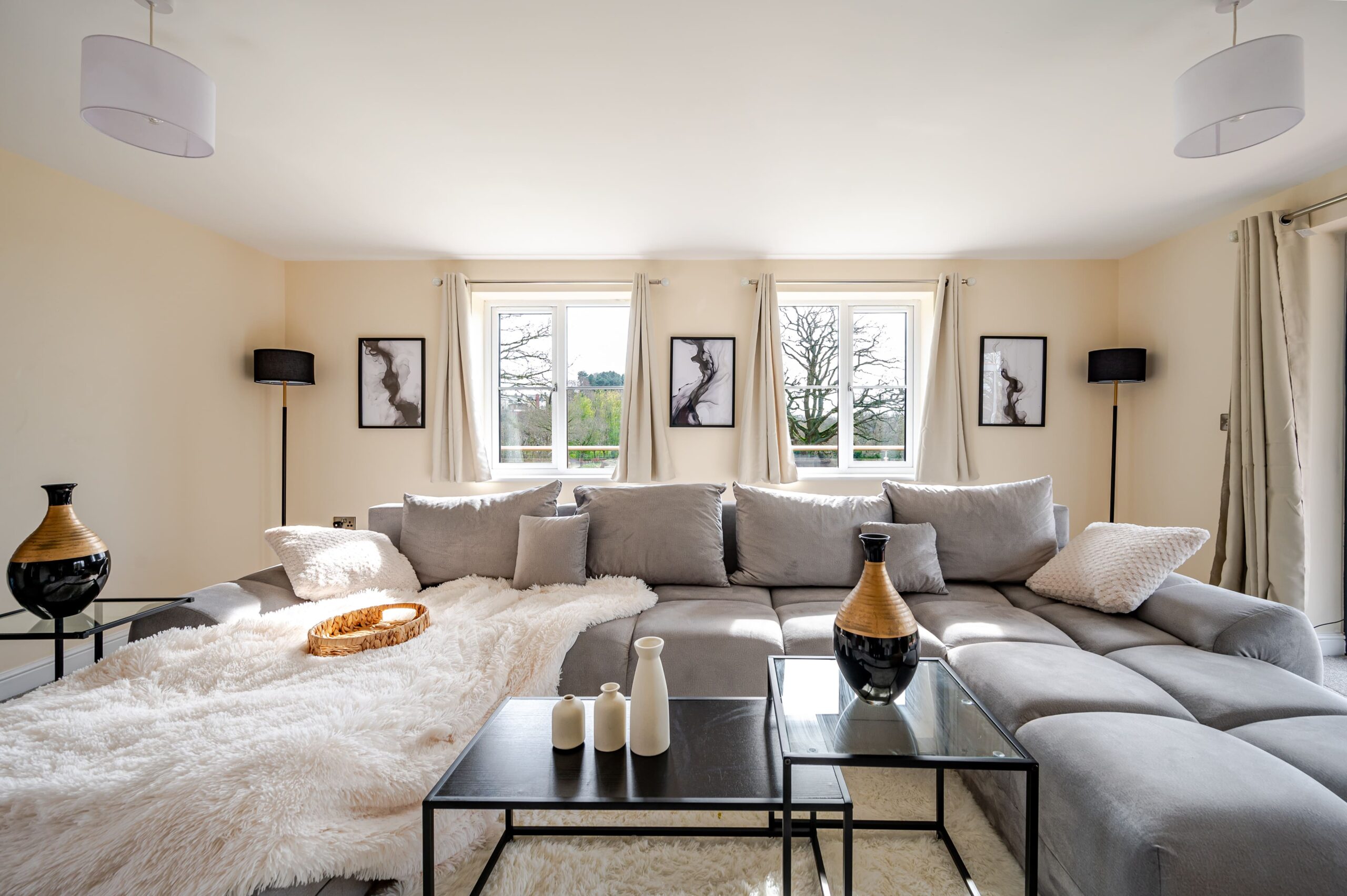 Modern living room with a large grey corner sofa, white fluffy throw, black coffee tables, and abstract wall art