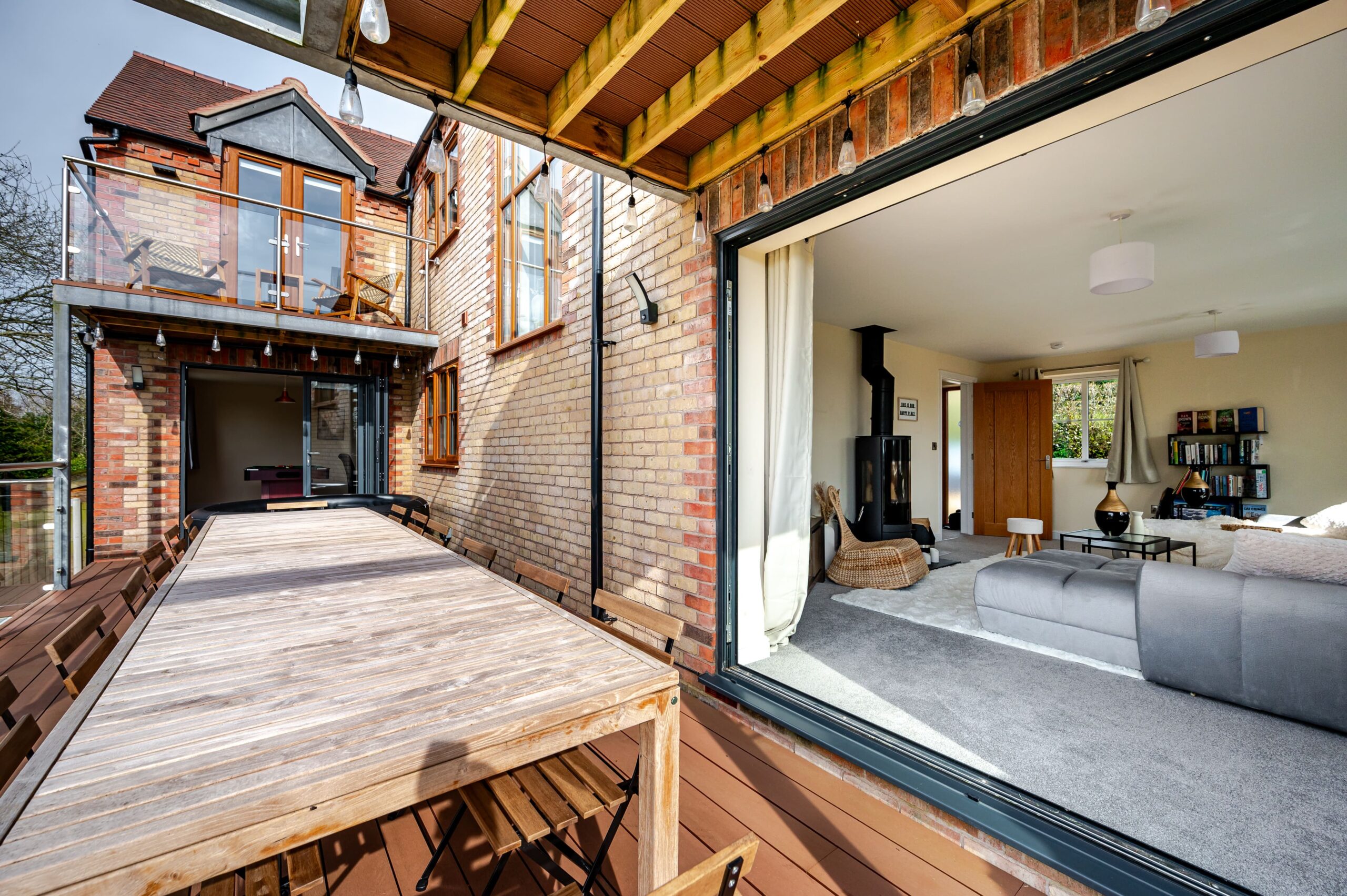 Wooden deck with a large dining table outside open sliding doors leading into a modern living room