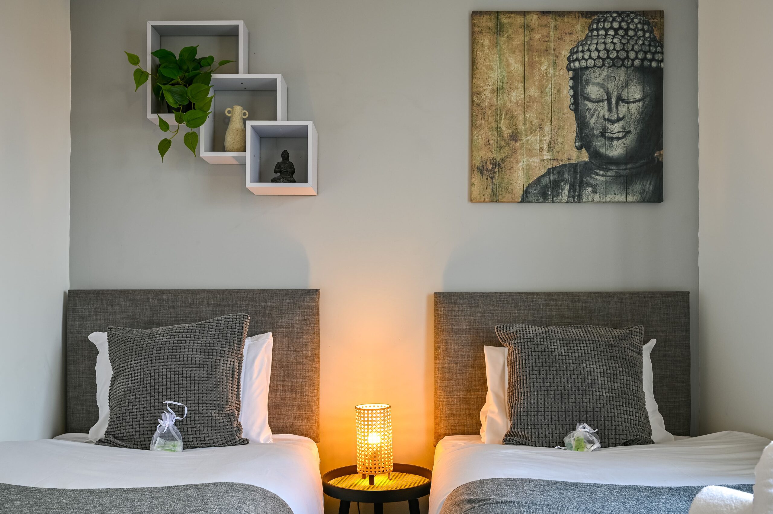 Twin bedroom with grey headboards, a warm bedside lamp, and Buddha wall art