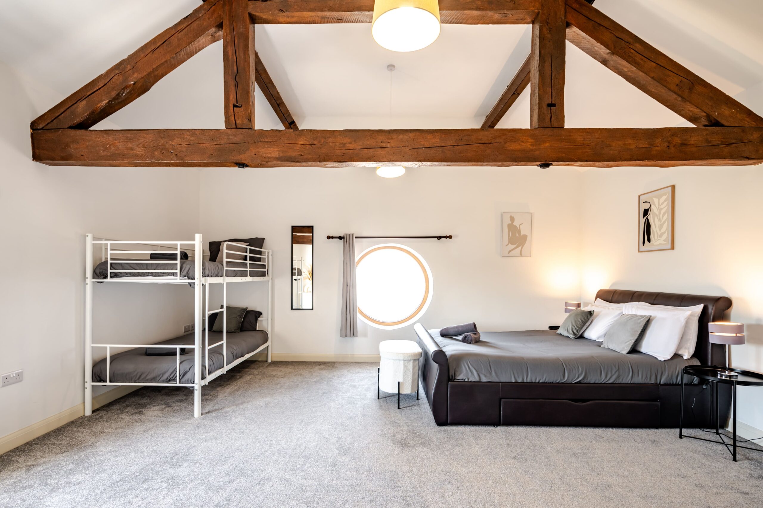 Bedroom with exposed wooden beams, a double bed, white metal bunk beds, and a circular window