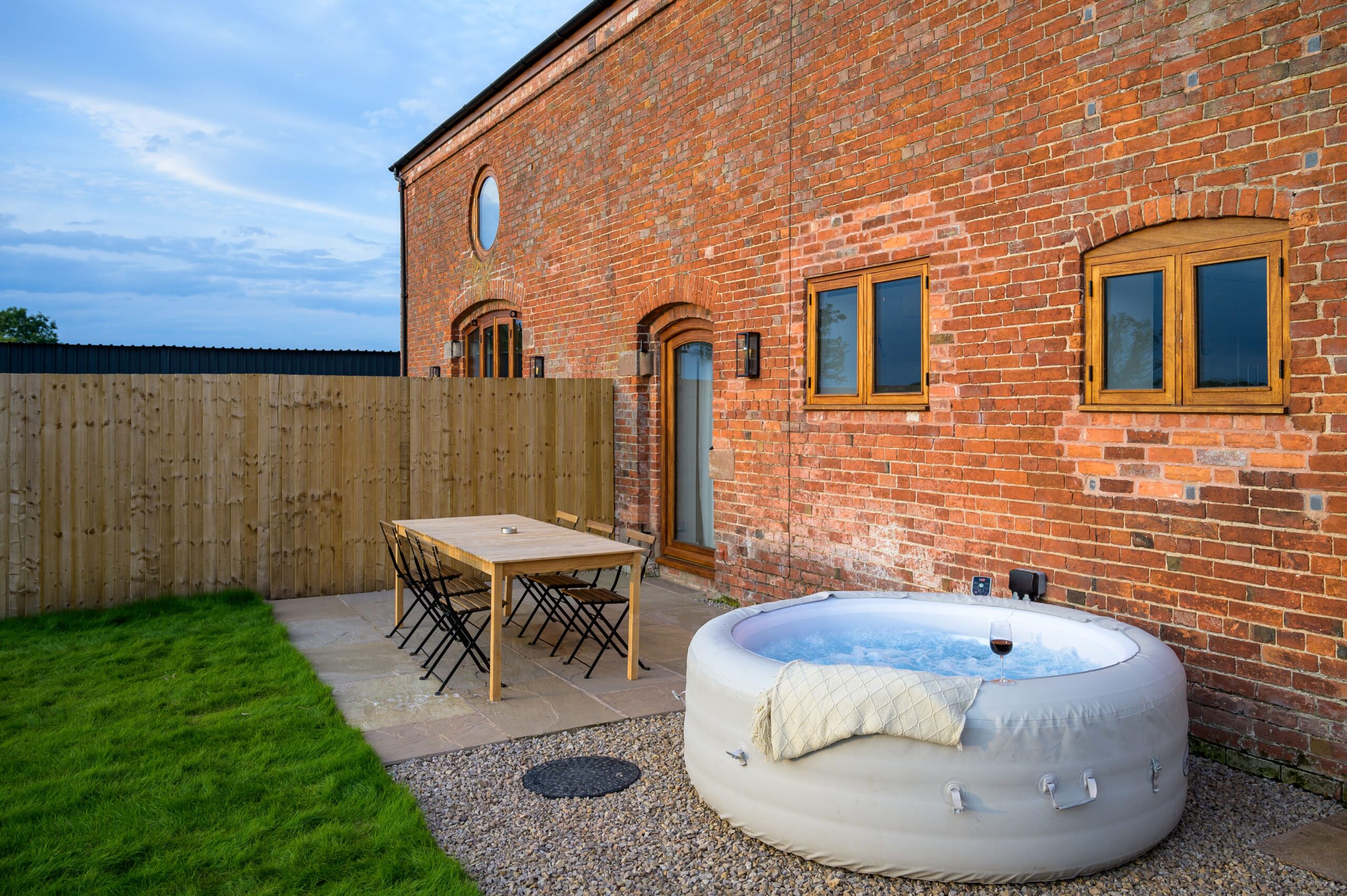 Patio area of a red brick building featuring a wooden dining table and an inflatable hot tub