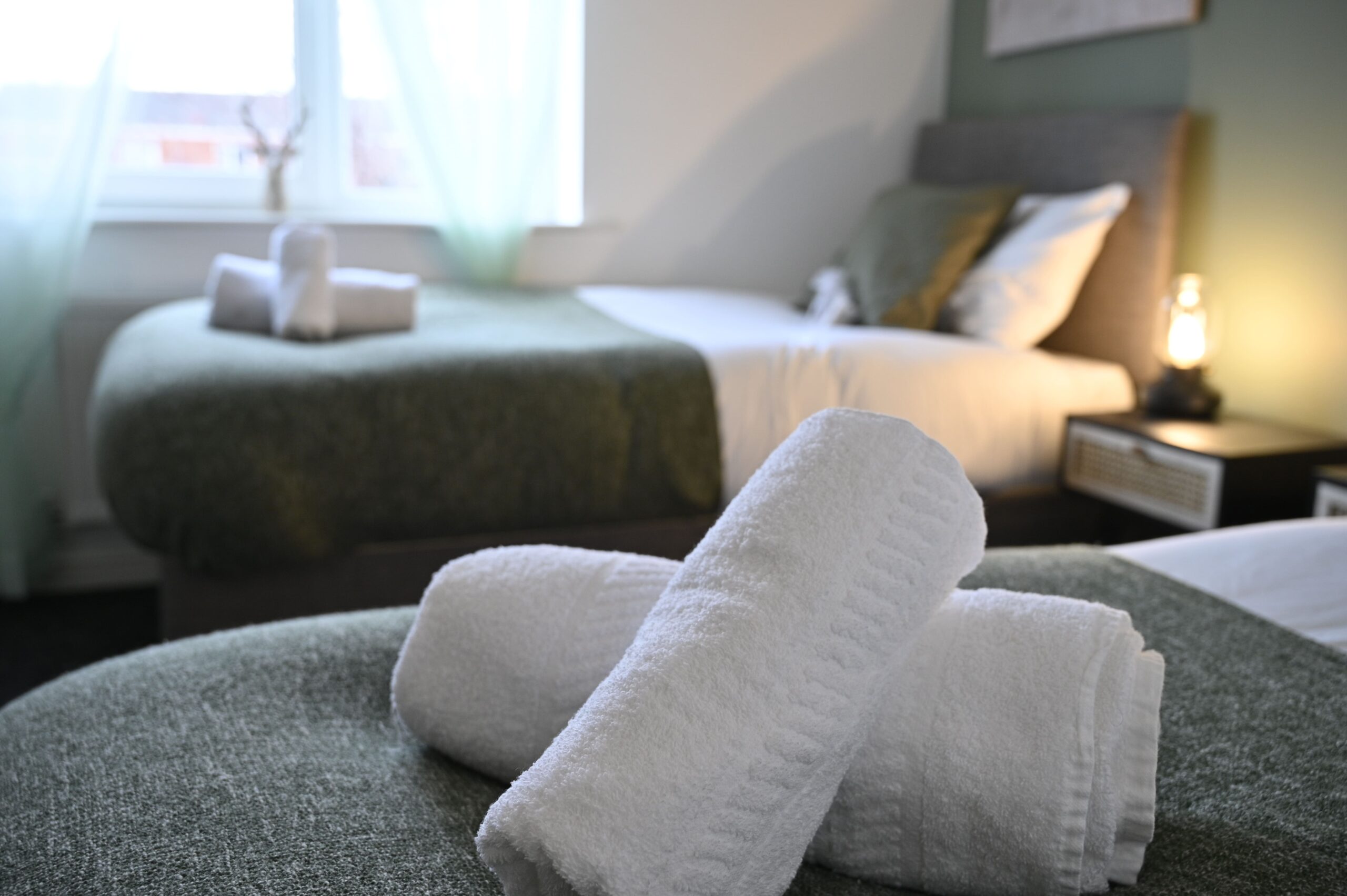 Rolled white towels on a bed with a green throw in a twin bedroom