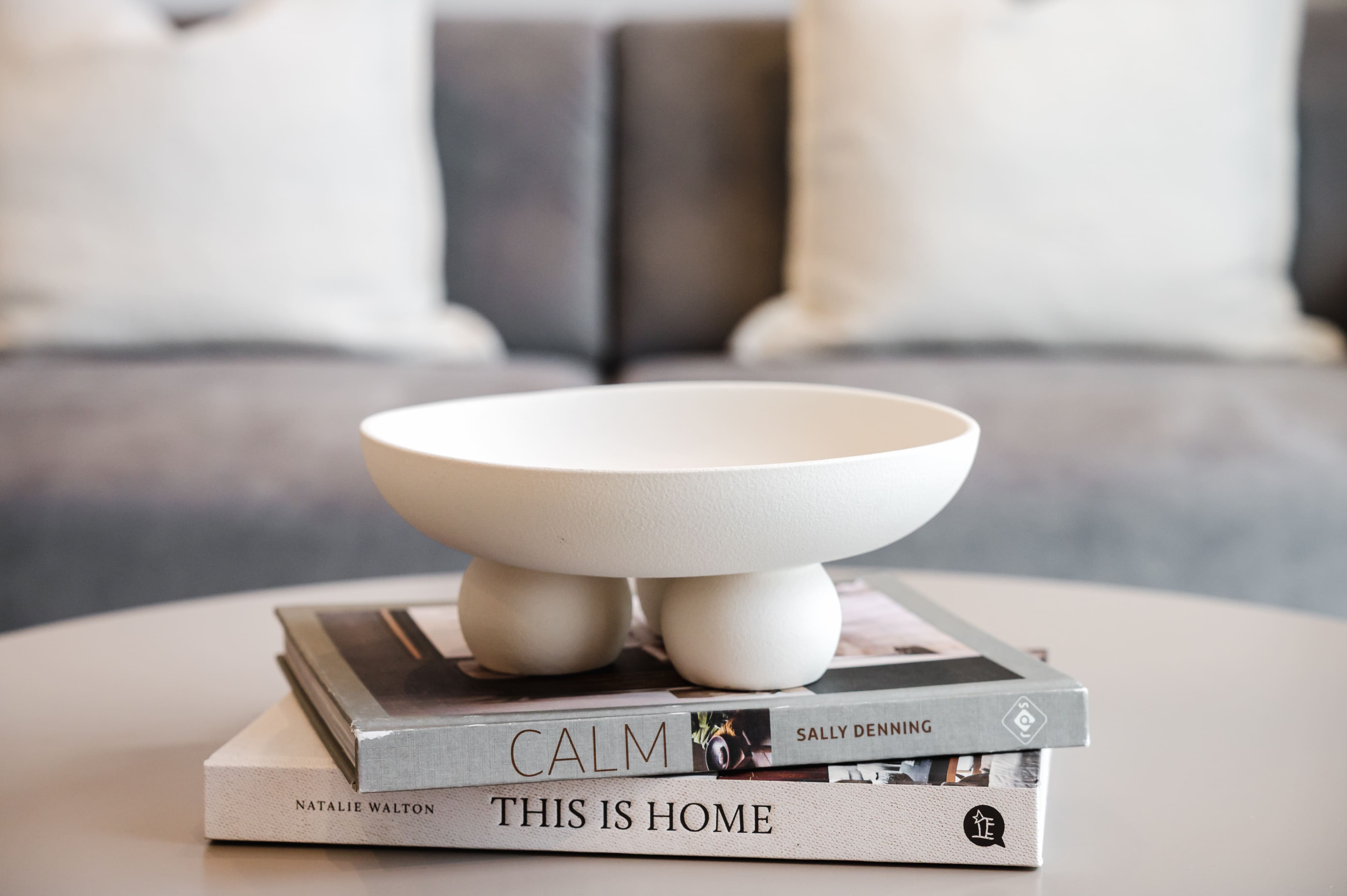 A white textured bowl with spherical feet sitting on a stack of coffee table books