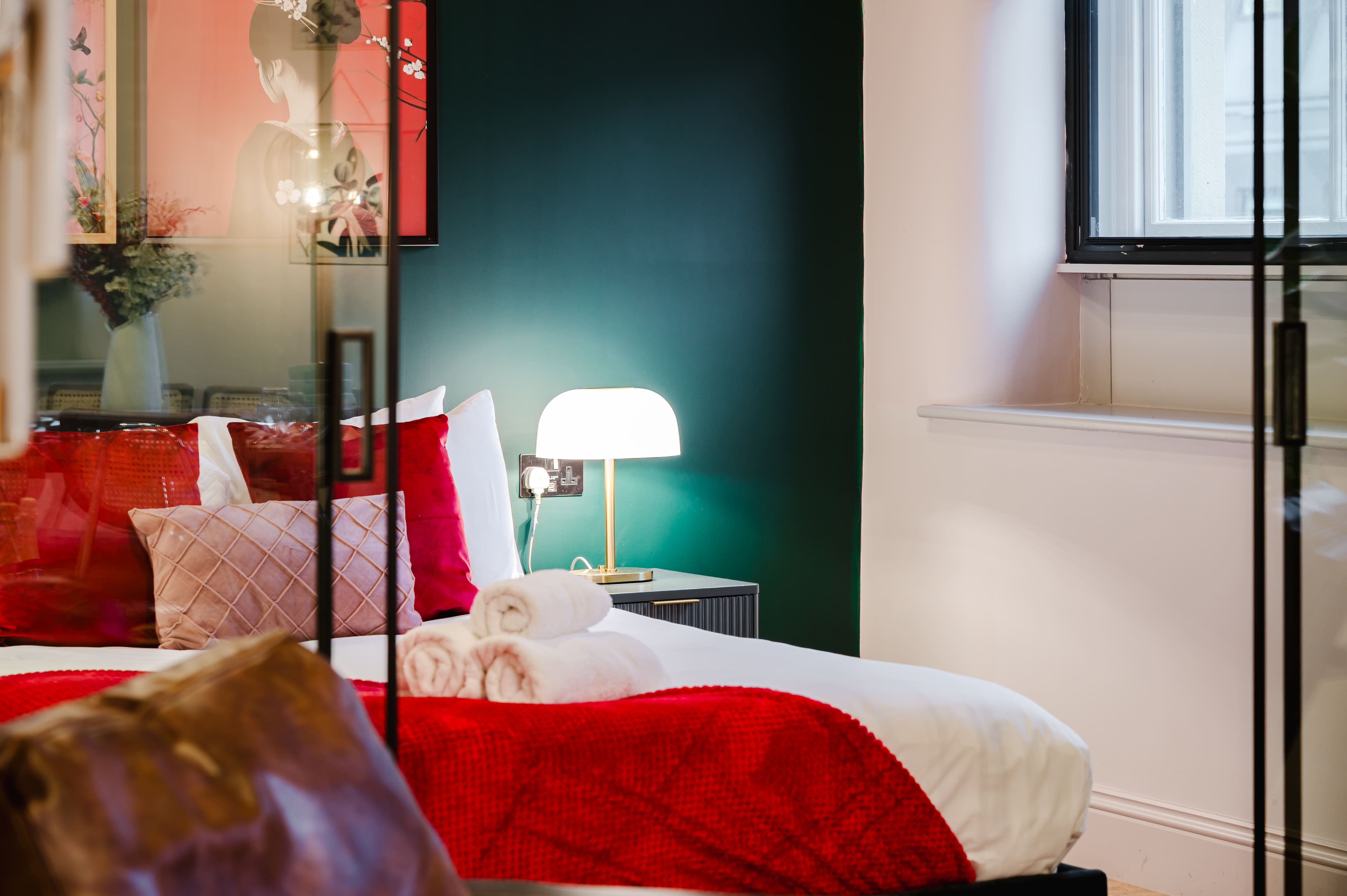 Stylish bedroom with a dark green feature wall, a bed with red cushions, and a lit lamp on a bedside table