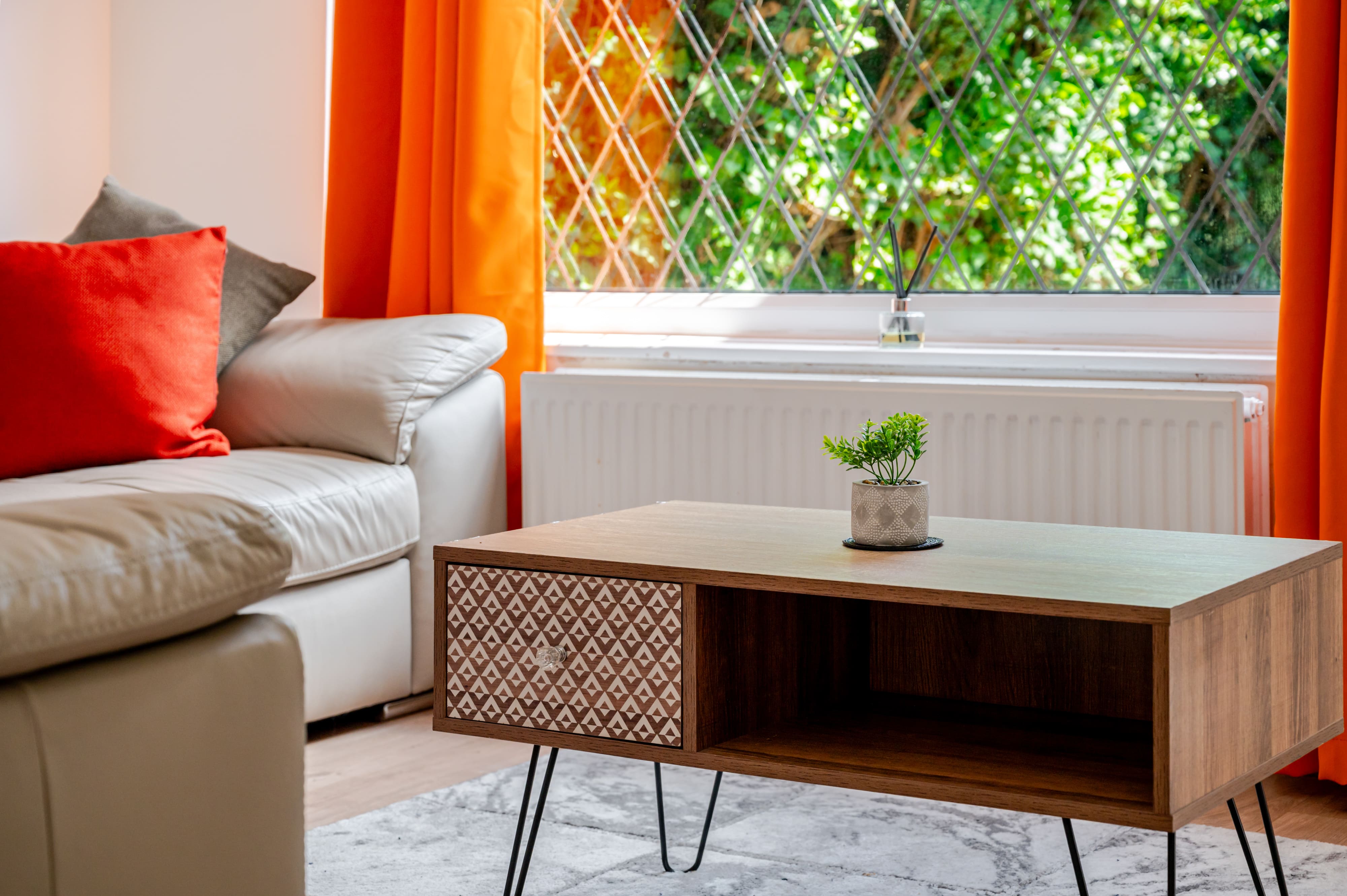 Wooden coffee table with a patterned drawer in a living room with orange curtains and a white leather sofa