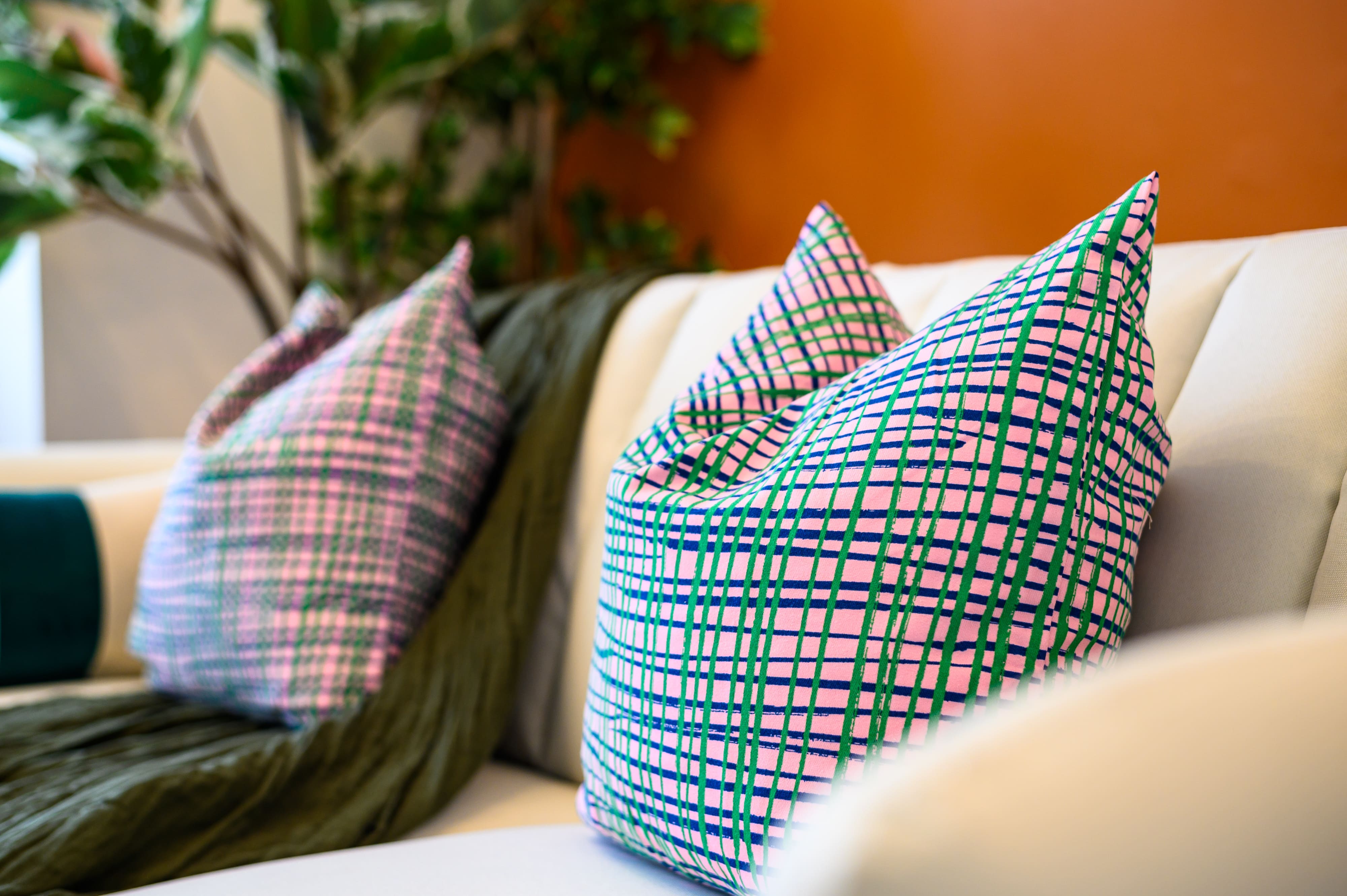 Two cushions with a pink and green grid pattern on a light-coloured sofa