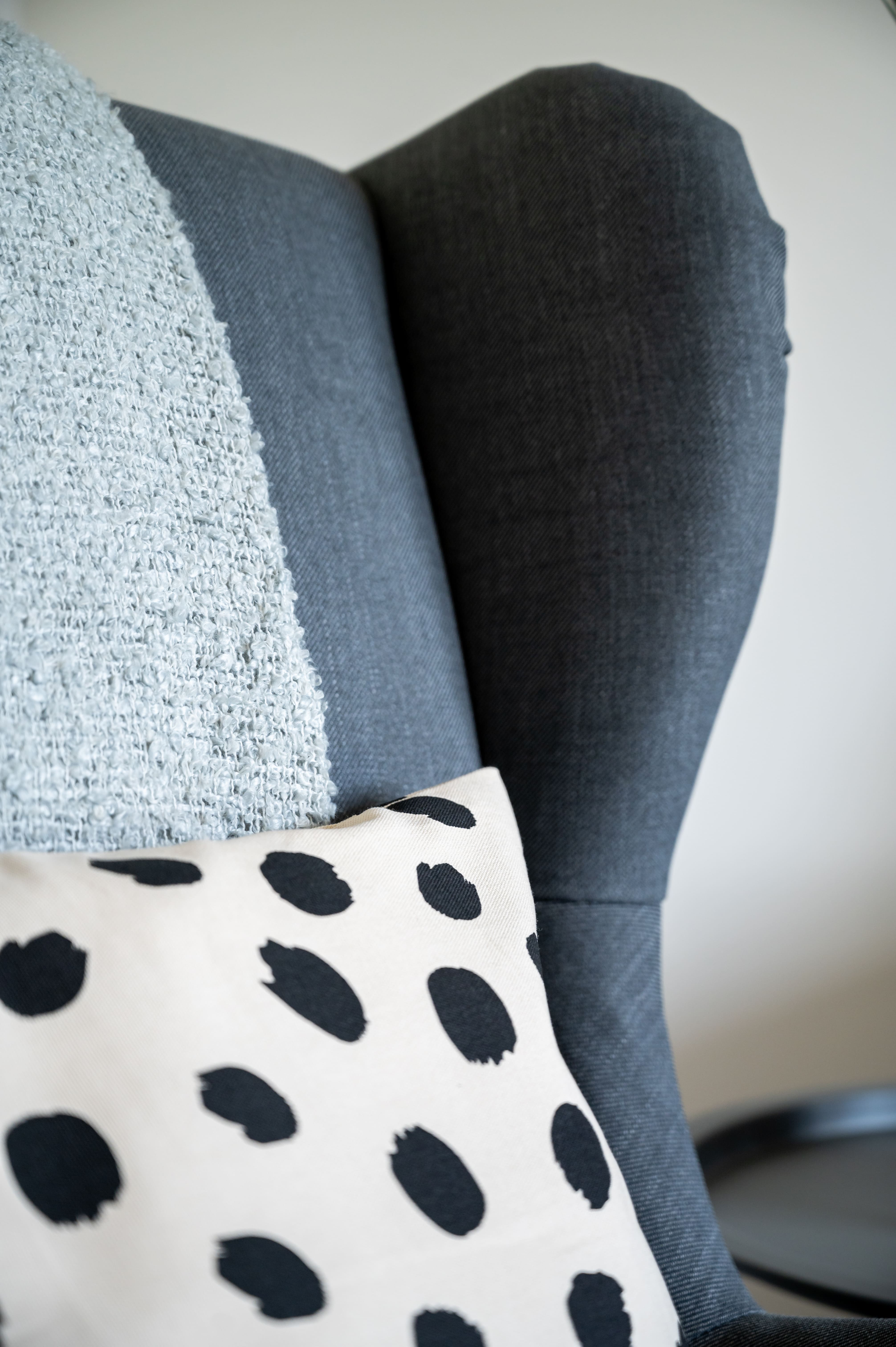 Close-up of a grey wingback armchair with a light blue textured throw and a black and white polka dot cushion