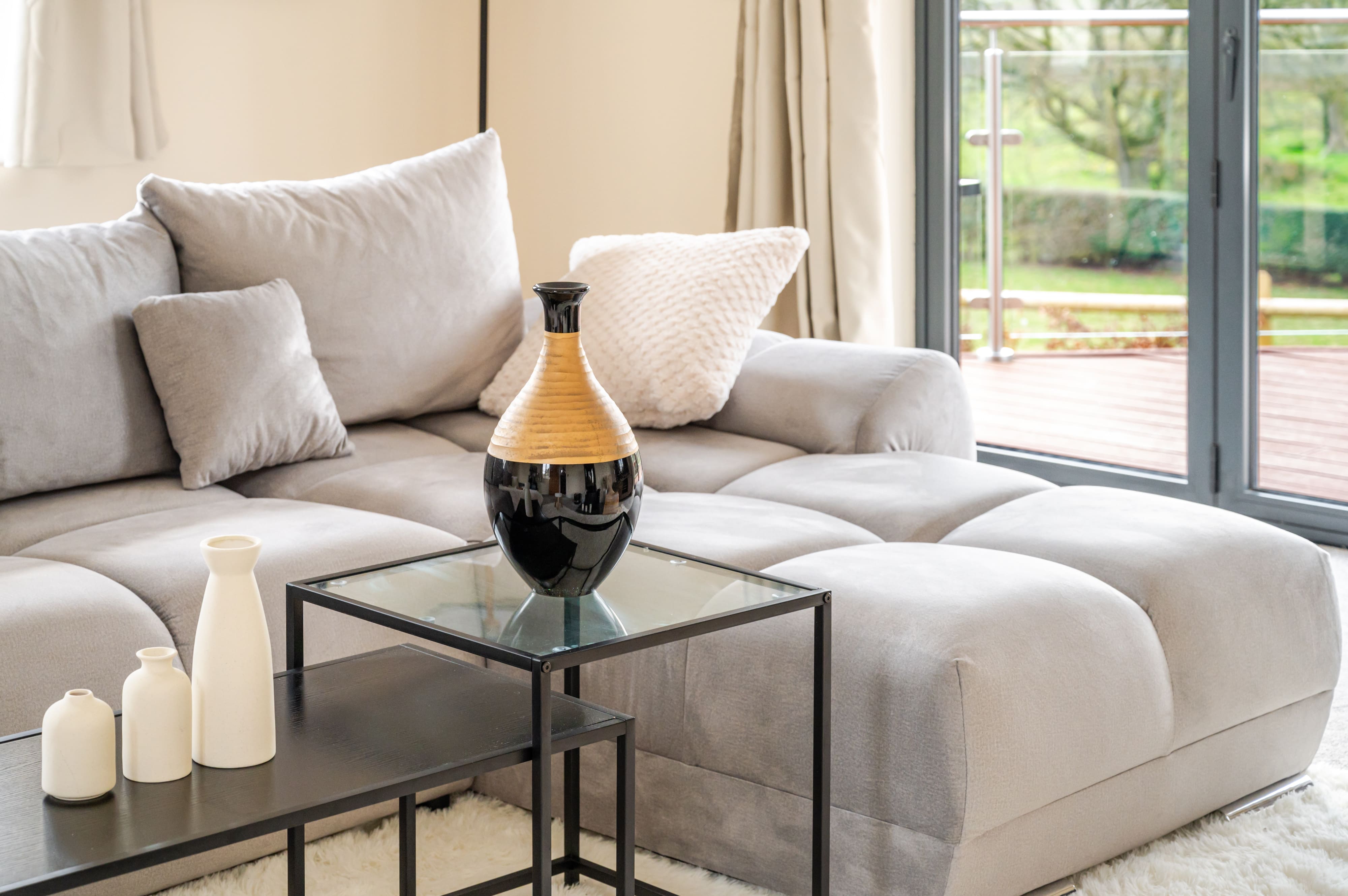 Modern living room with a grey L-shaped sofa, glass nesting tables, and decorative vases